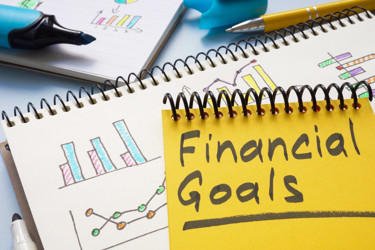 Notebook with the words 'Financial Goals' on a yellow page, surrounded by colorful graphs and charts, representing the importance of setting realistic financial goals for effective financial planning.